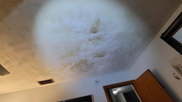 A light shines on a stained ceiling of a residential house.