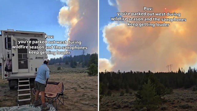 A person stands near an RV, watching a large cloud of smoke in a forested area during wildfire season.