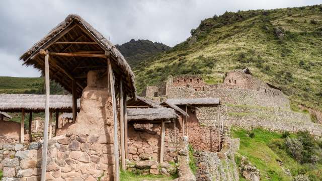 A cluster of ancient stone structures and thatched huts situated on a hillside, surrounded by lush greenery.