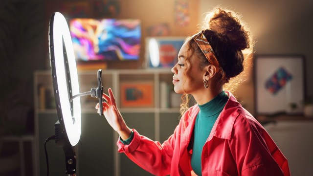 A woman adjusts her smartphone in a ring light.