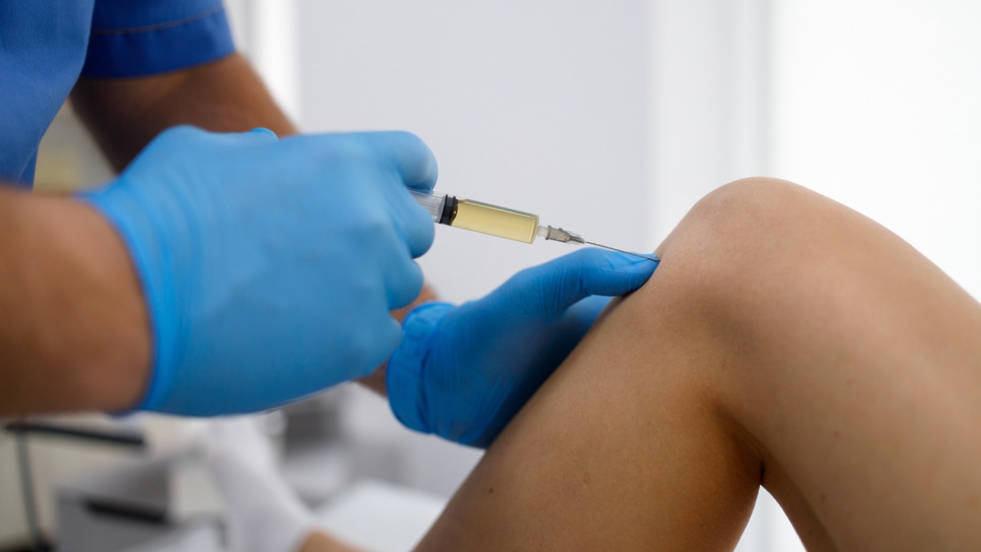 A healthcare professional injecting medicine into a person's knee.
