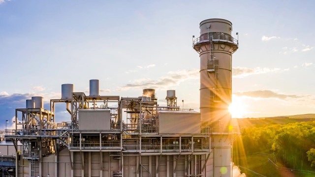 A power plant with large machinery and a smokestack at sunset.