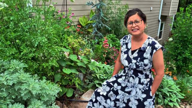 A woman in a floral dress sits in a vibrant garden.