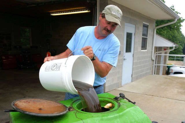 A man pouring dark liquid from a bucket into a green tank.