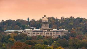 A historic government building surrounded by colorful autumn trees against a pastel sky.