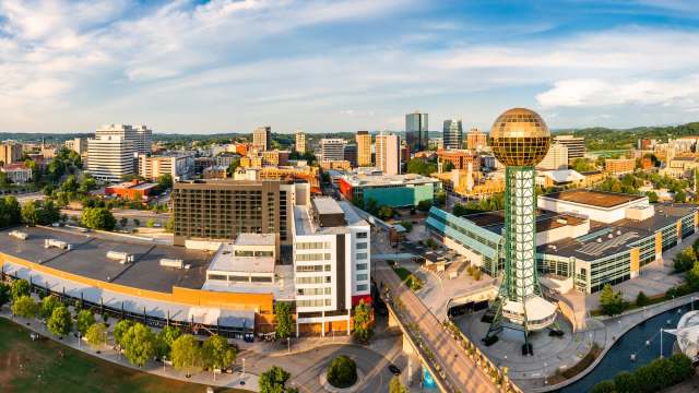 A panoramic view of the Knoxville, Tennessee, skyline featuring the Sunsphere tower and various buildings under blue skies.