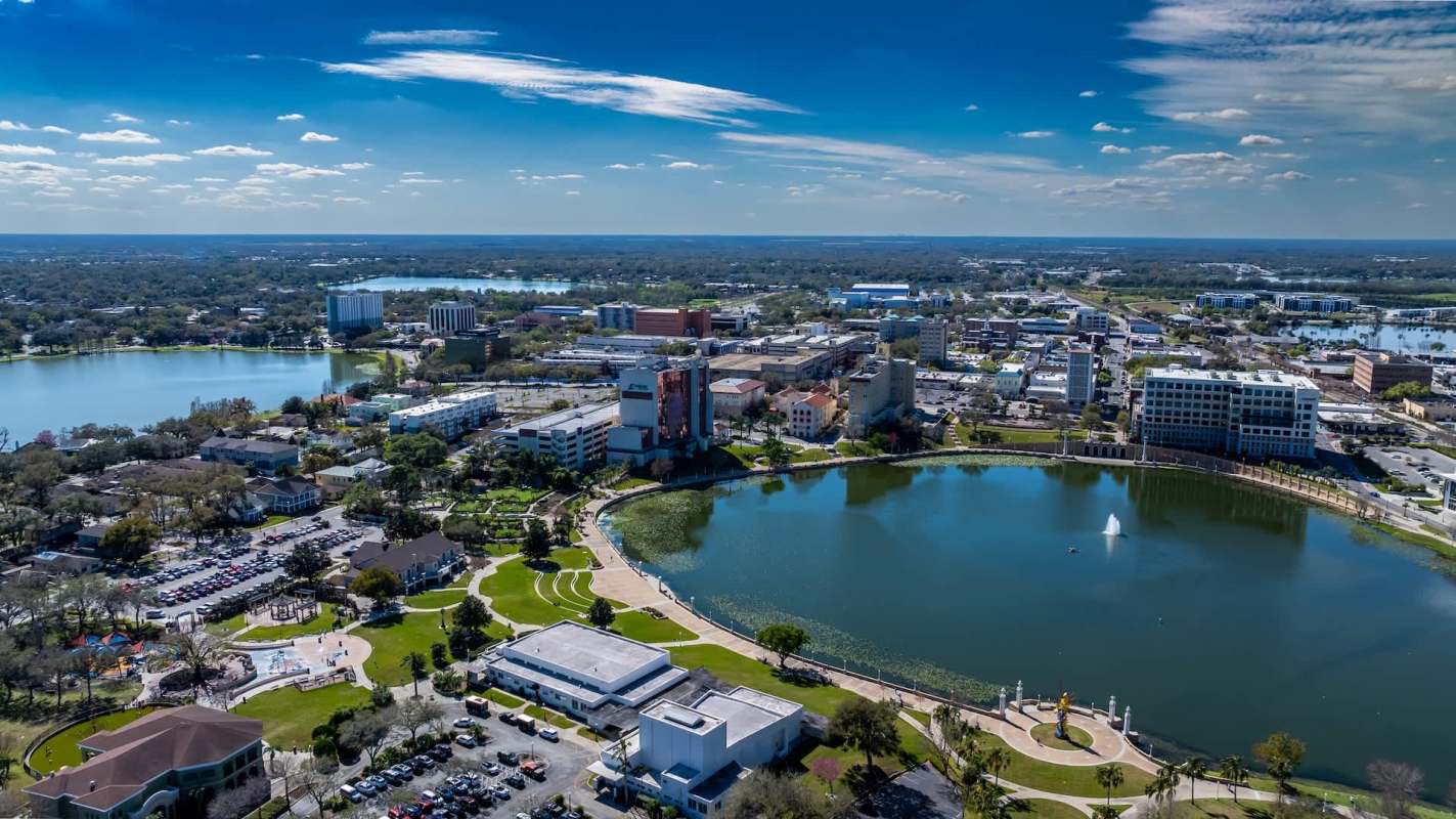 Aerial view of a lake surrounded by urban development and parks under a blue sky.