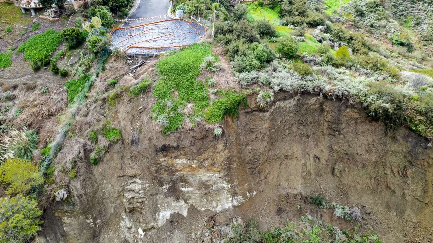 A landslide reveals soil and vegetation near a road under construction.