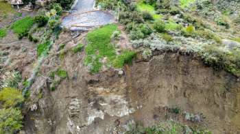A landslide reveals soil and vegetation near a road under construction.