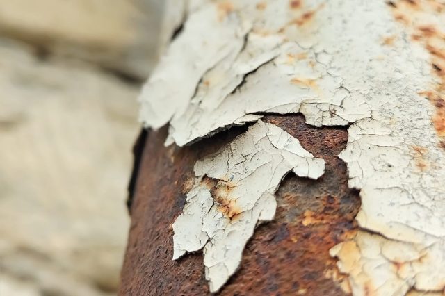 Close-up of peeling paint revealing rust underneath on a metal surface.