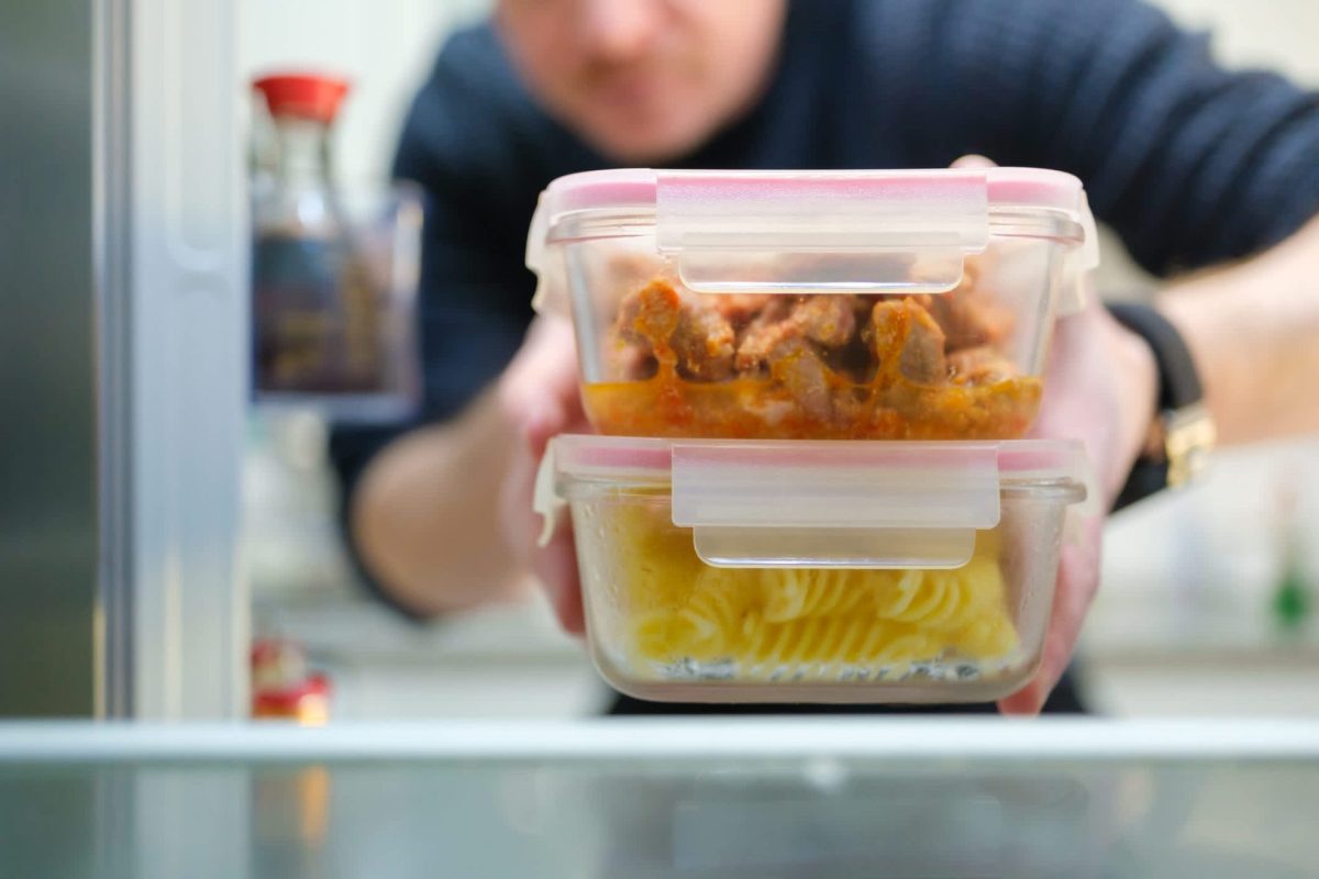 A person reaching for two stacked glass meal prep containers in a refrigerator.