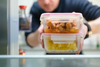 A person reaching for two stacked glass meal prep containers in a refrigerator.