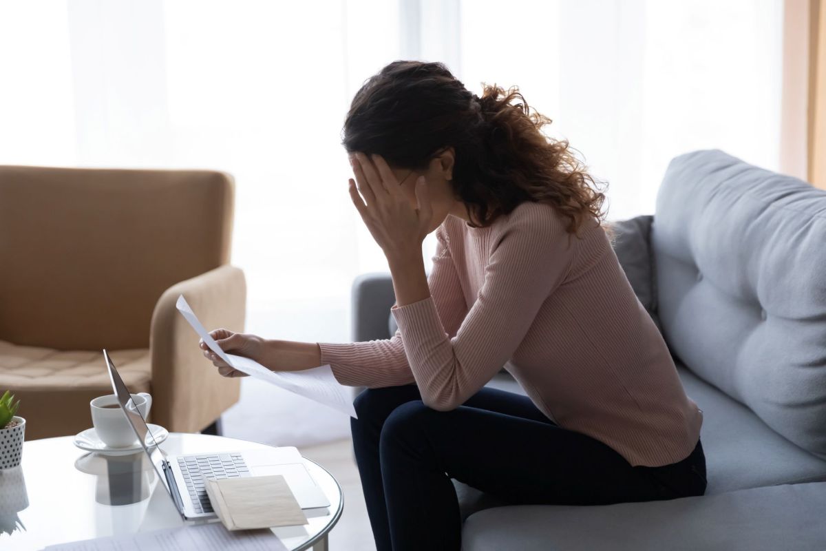 A woman sitting on a sofa appears distressed while looking at papers.