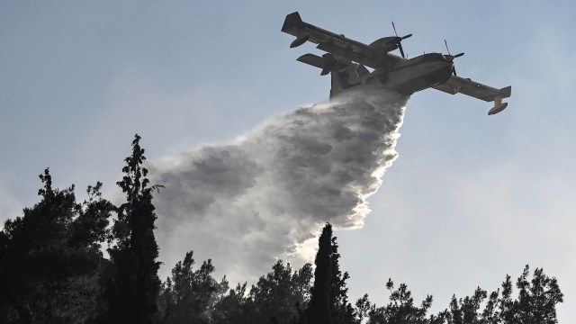 A firefighting aircraft releases water over trees to combat a wildfire.