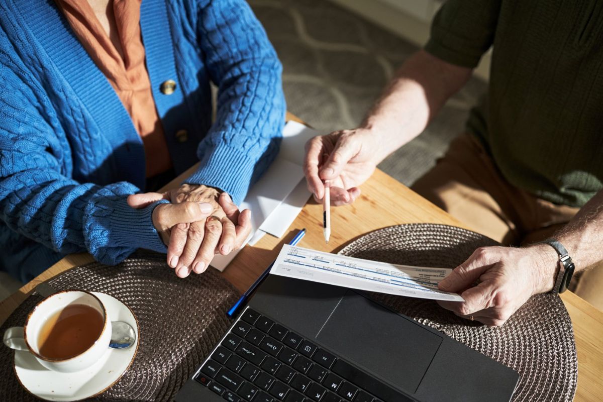 An elderly person holds hands with another person, reviewing documents.
