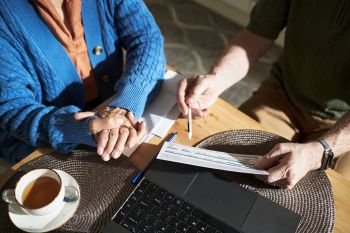An elderly person holds hands with another person, reviewing documents.