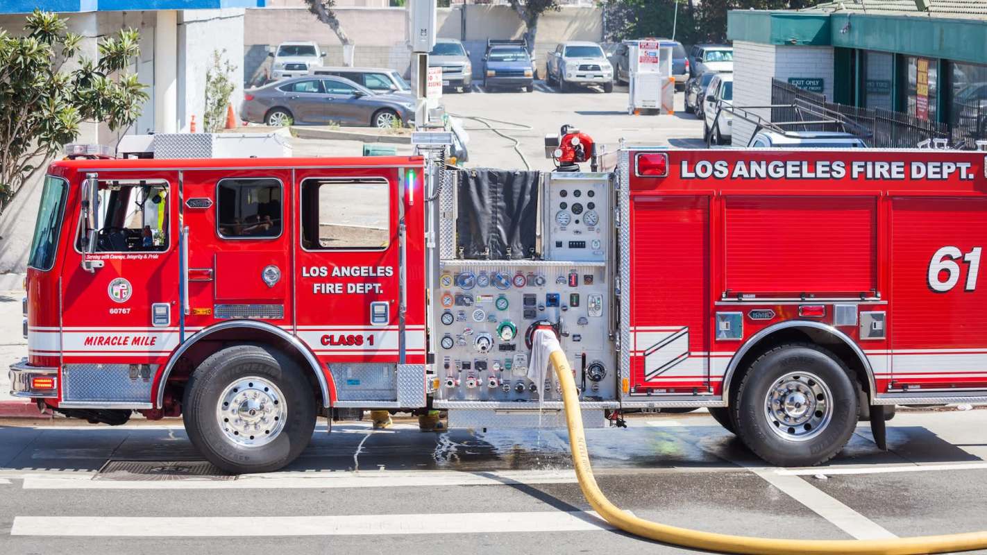 A Los Angeles Fire Department fire truck with hoses and equipment parked in an urban area under bright sunlight.