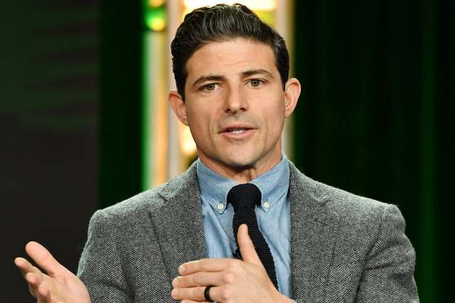CBS News anchor Matt Gutman, in a gray blazer, speaks while gesturing with his hands.