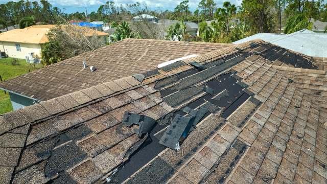 A damaged roof with missing shingles and exposed underlayment, viewed from an elevated angle.