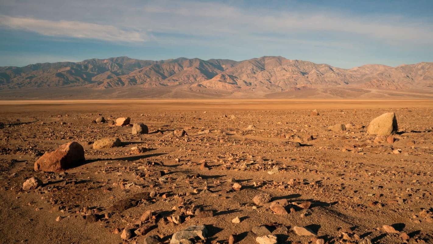 A barren landscape with scattered rocks and distant mountains under a clear sky.