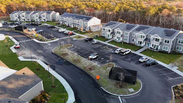 An aerial view of a residential complex with multiple buildings and parking areas surrounded by trees.
