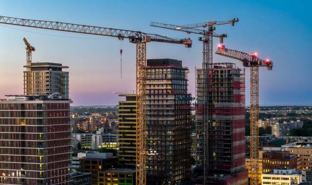 A city skyline under construction with multiple cranes against a twilight backdrop.