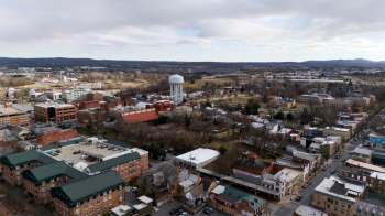 An aerial view of a small town featuring buildings, a water tower, and distant hills under a cloudy sky.