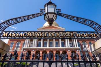 The Massachusetts State House features a golden dome and historic brick architecture behind an ornate gate.