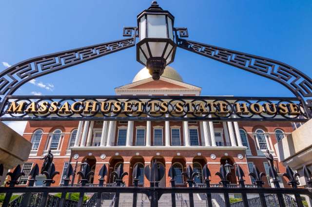 The Massachusetts State House features a golden dome and historic brick architecture behind an ornate gate.