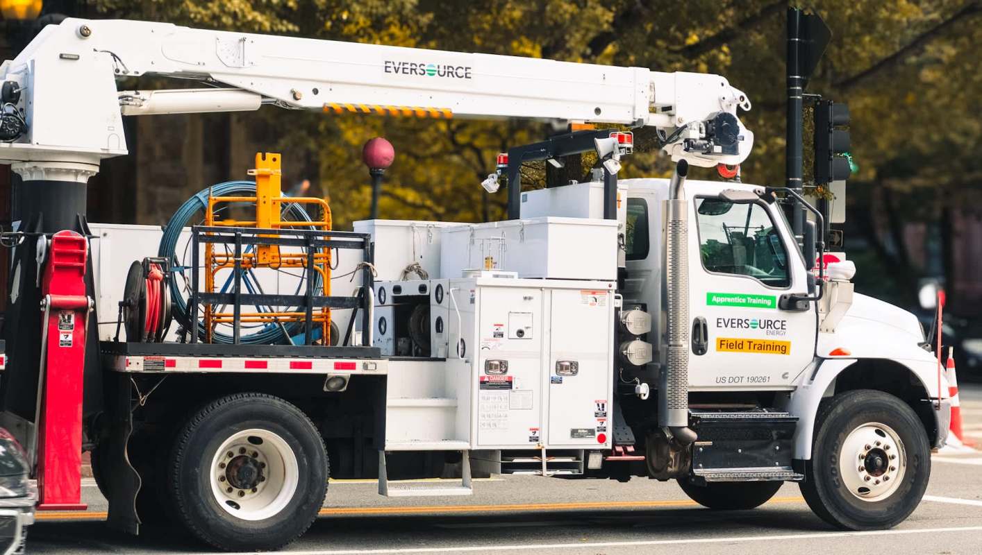 An Eversource utility truck with a raised bucket and equipment for electrical maintenance parked on a city street.
