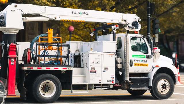 An Eversource utility truck with a raised bucket and equipment for electrical maintenance parked on a city street.