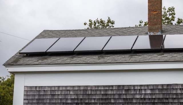 A roof with solar panels installed beside a brick chimney and wooden shingles.