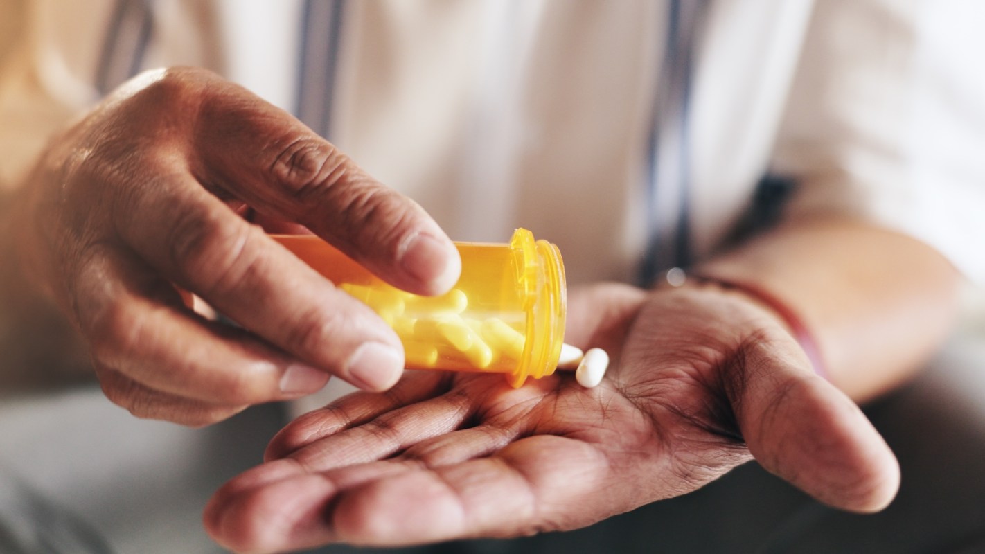A person pours pills from an orange prescription bottle into their hand.