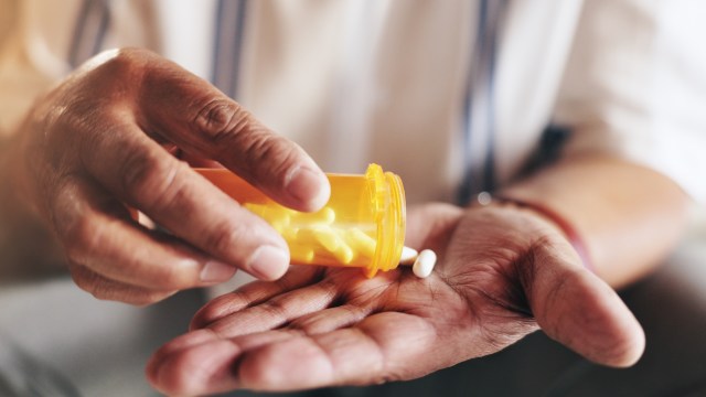 A person pours pills from an orange prescription bottle into their hand.