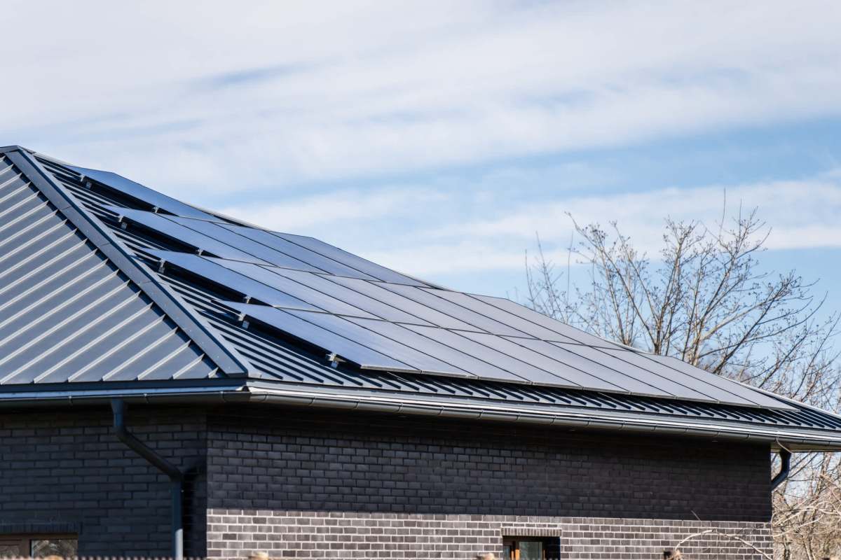A close-up of a black roof with solar panels under a clear blue sky.