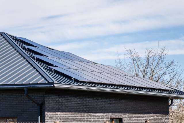 A close-up of a black roof with solar panels under a clear blue sky.
