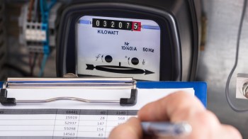 A close-up of an electric meter displaying a reading of 30275 kilowatts next to a clipboard with data.