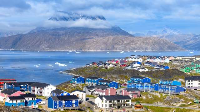 A colorful settlement with houses beside a serene fjord, surrounded by mountains and icebergs.