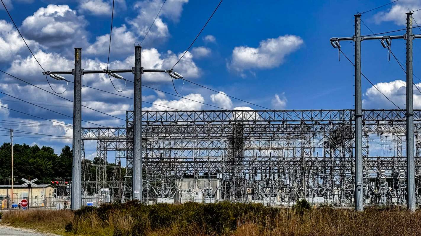 An electrical substation with power lines and a blue sky filled with clouds.