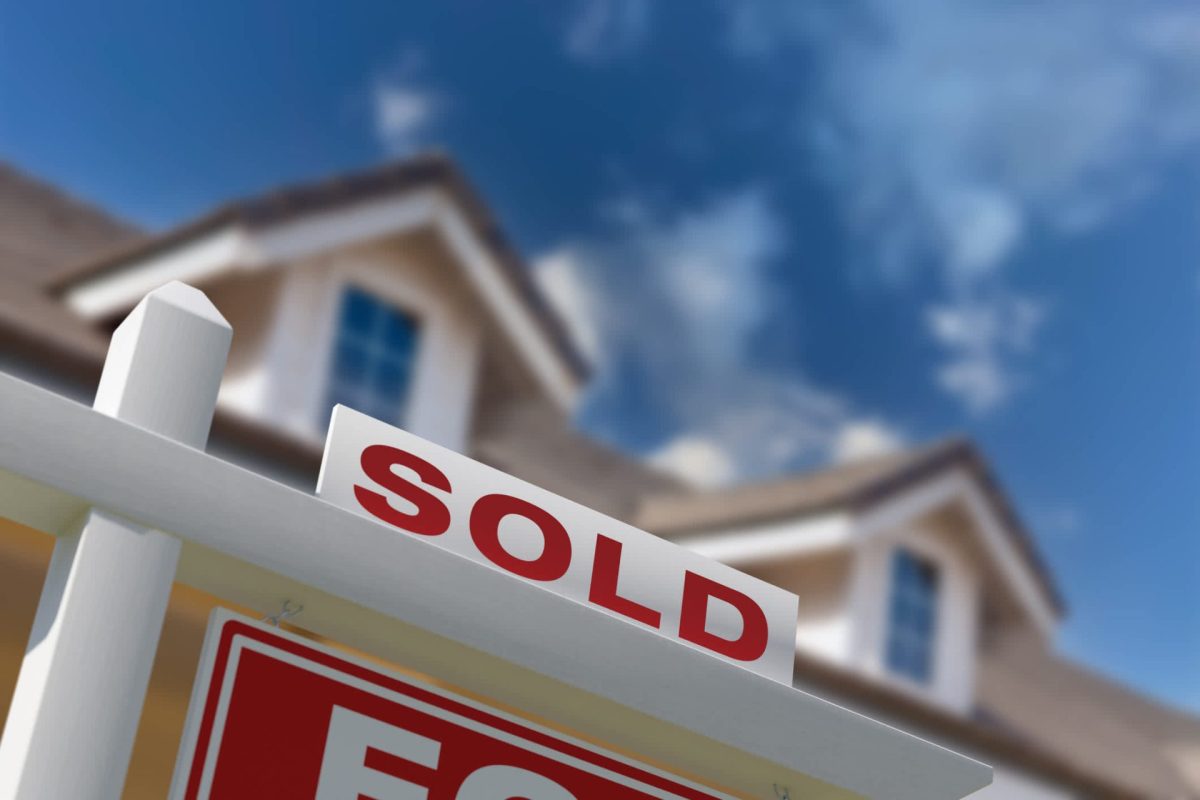 A "Sold" sign displayed prominently in front of a house against a blue sky background.