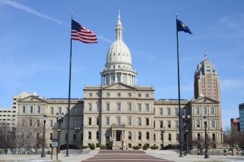 The Michigan State Capitol building with flags flying, surrounded by a clear blue sky.