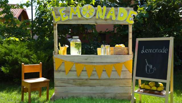 A lemonade stand with a chalkboard sign and decorative yellow flags.