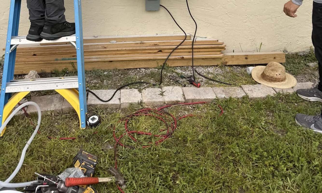 The outside of a house with a ladder and cables visible against the wall.