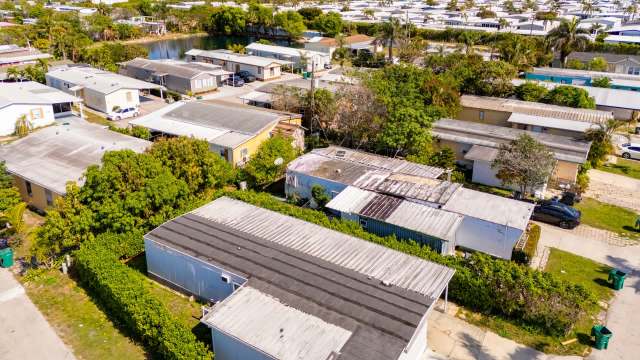 An aerial view of a residential area featuring mobile homes, greenery, and a small pond in the background.