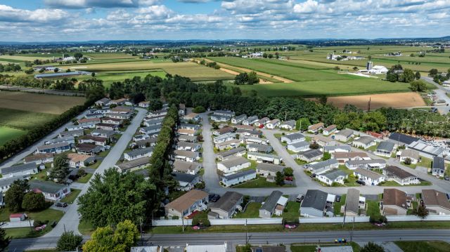 Aerial view of a mobile home community surrounded by agricultural fields and distant hills under a cloudy sky.