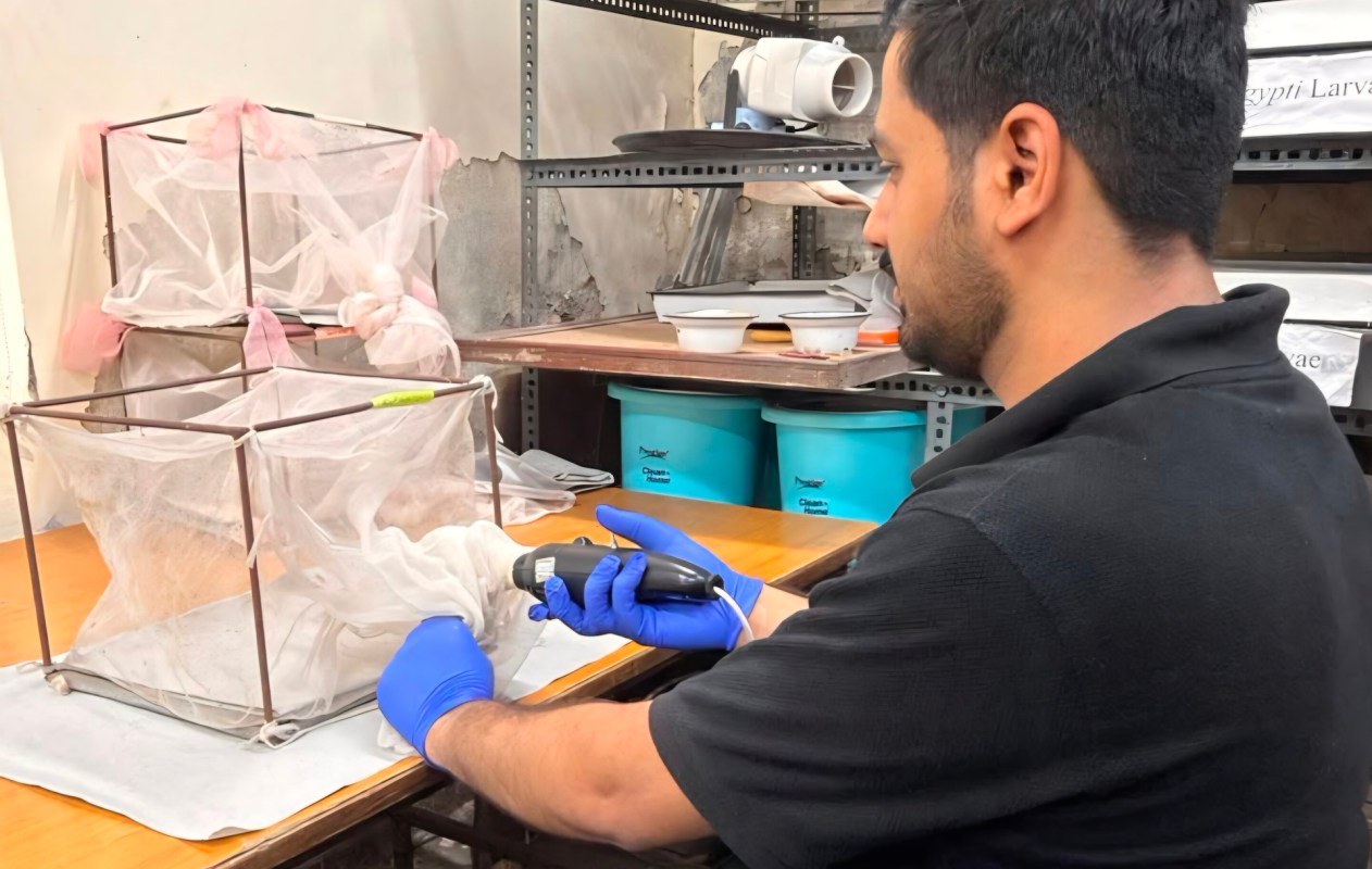 A person uses a handheld device to manipulate materials in a lab setting with insect enclosures.
