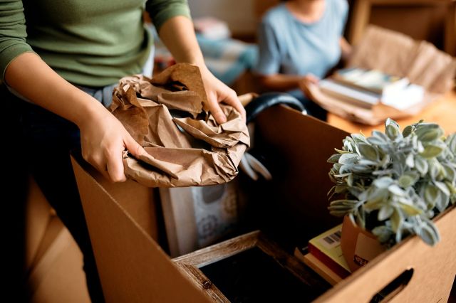 A woman putting items into a moving box.