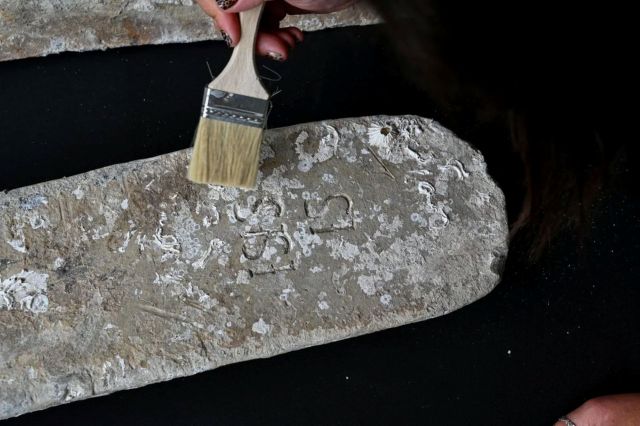A person brushes dust off an ancient stone tablet with visible inscriptions and marine fossils.