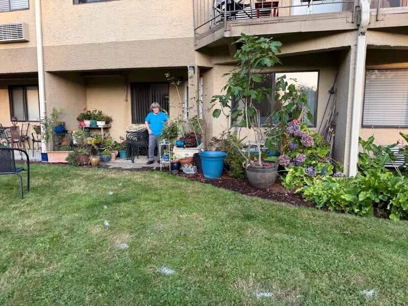 A women standing near a garden strip with potted plants and flowers.