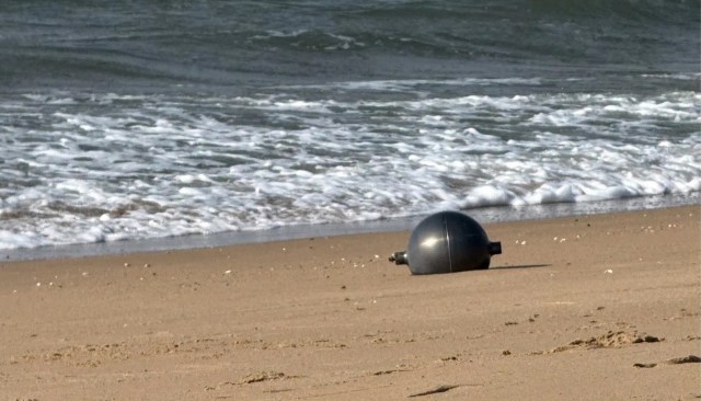 A metallic orb rests on a sandy beach with gentle waves lapping in the background.